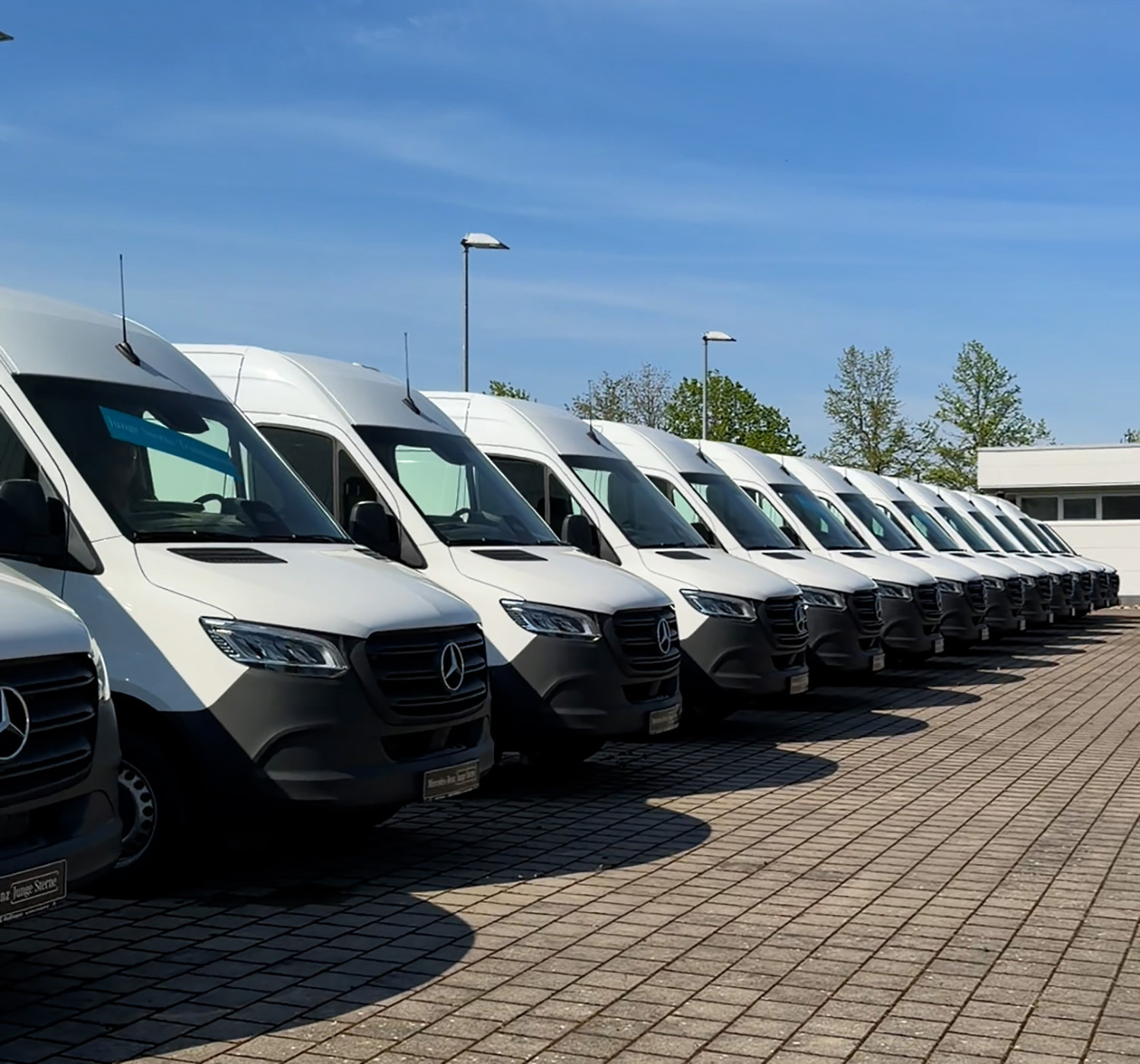 Zehn weiße Mercedes-Benz Sprinter stehen auf Hof